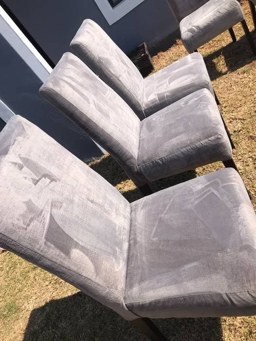 A row of upholstered dining chairs drying outdoors after cleaning.